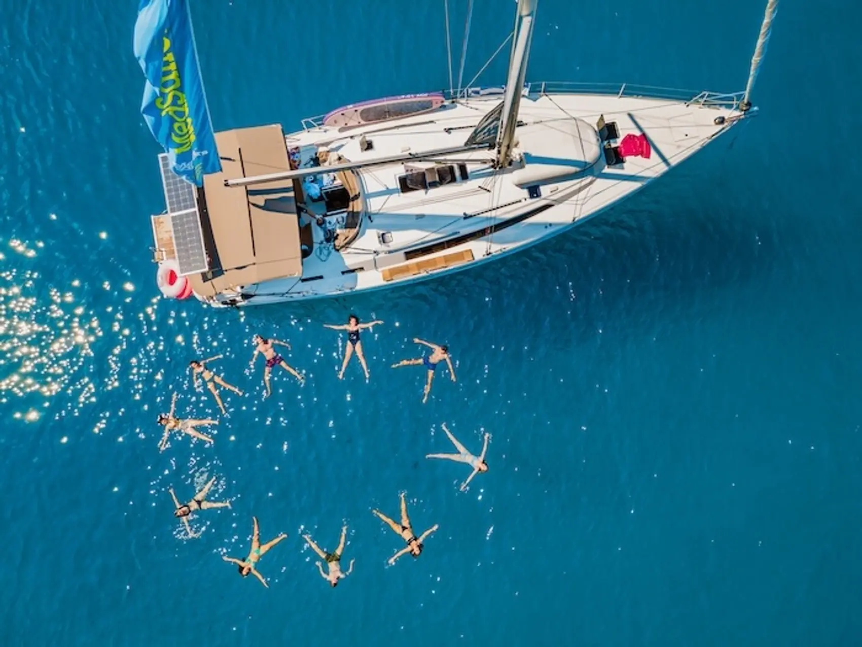 Photo of group of people swimming in a star shape near a sailing yacht in the Mediterranean.
