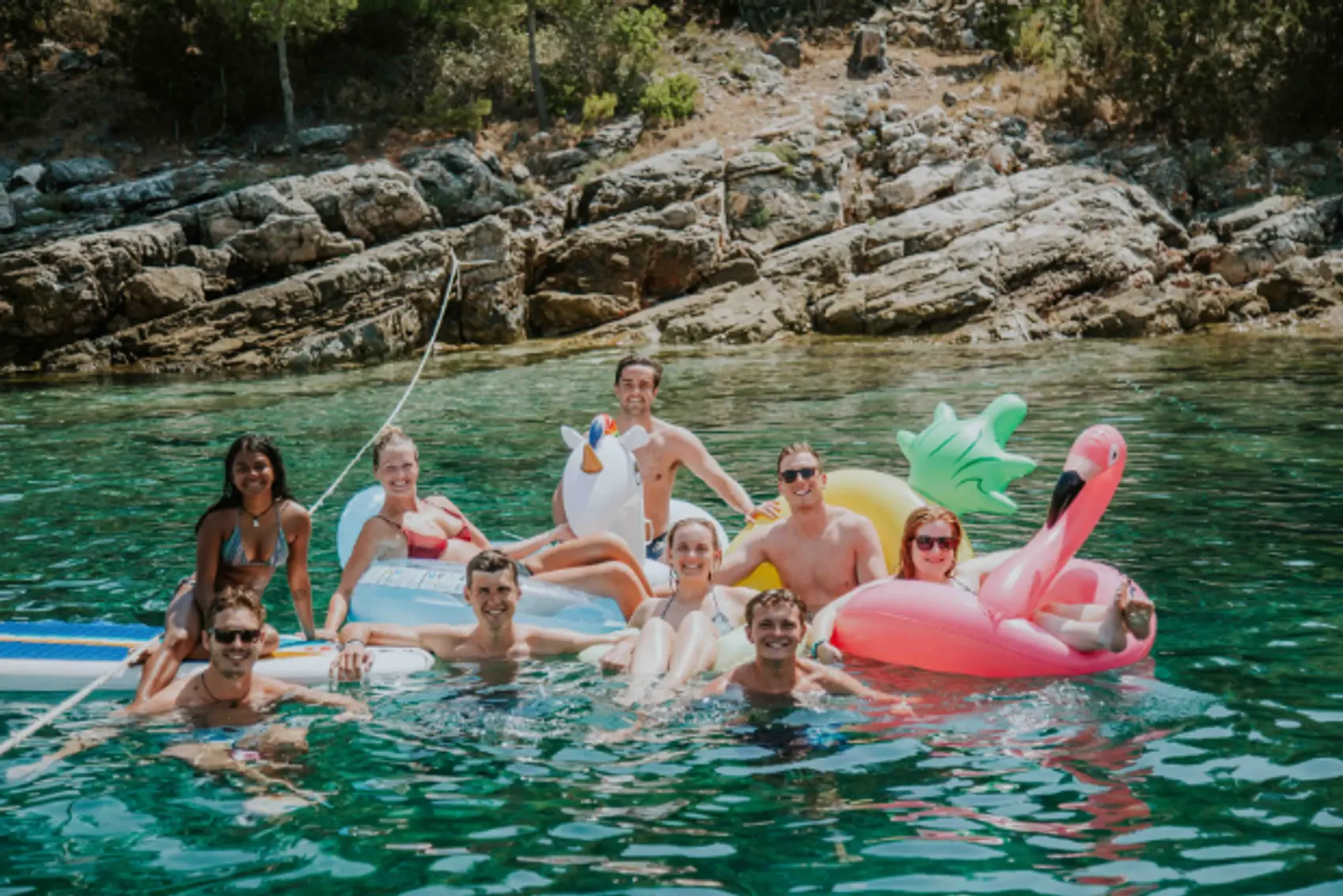 A group of young travellers in floaties in a beautiful bay in the Mediterranean.